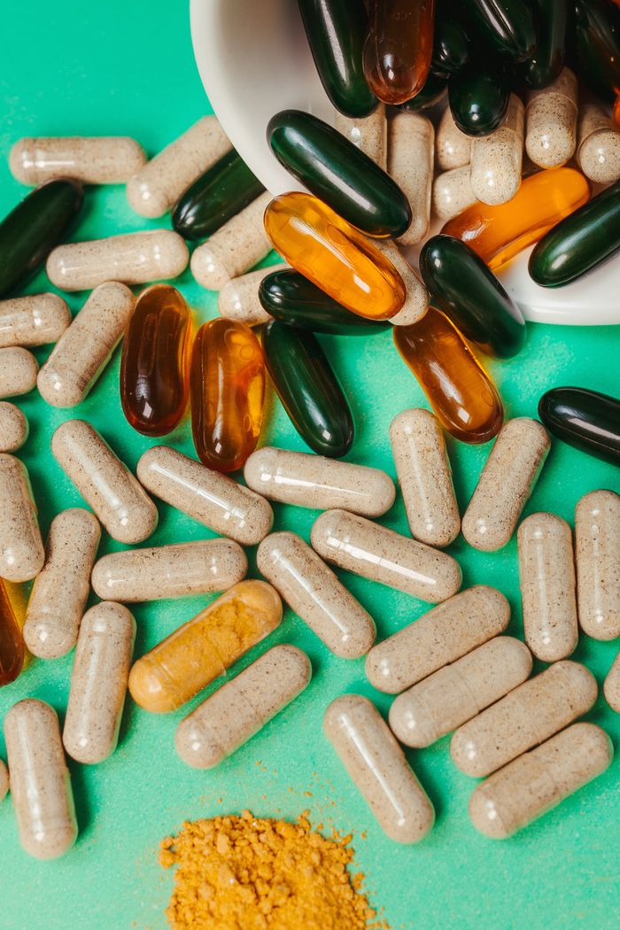 Close-up of various vitamins and supplements scattered on vibrant green surface.